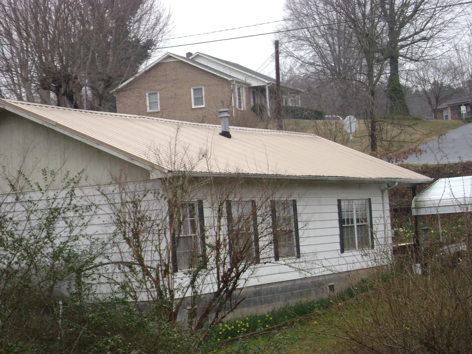 Tan metal roof on a white sided house set into a hillside — Commercial Roofing by Roofing Brothers in Lumberton