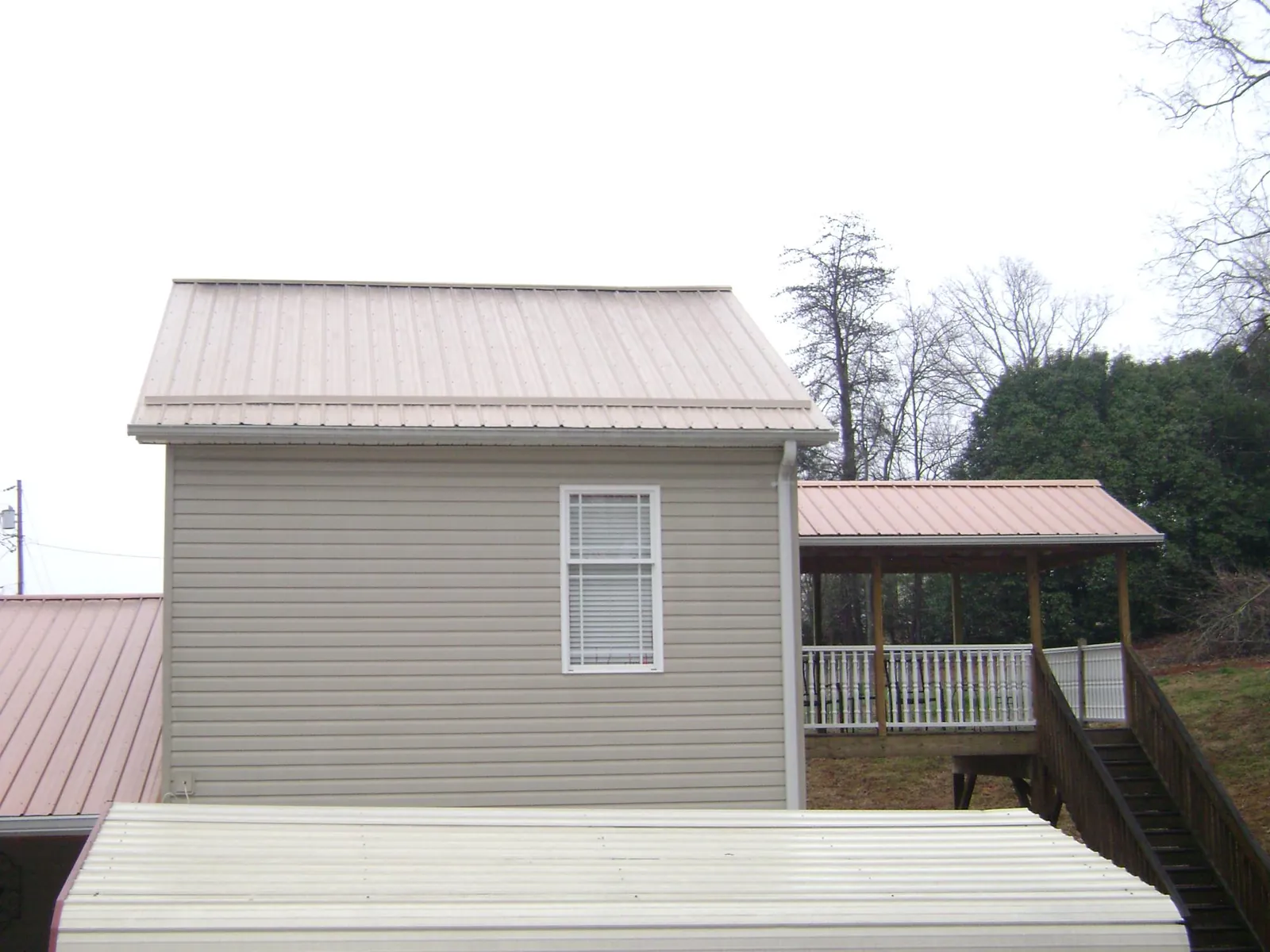 Tan metal roofs on a two story addition and attached porch, from a Roof Replacement job in Lumberton