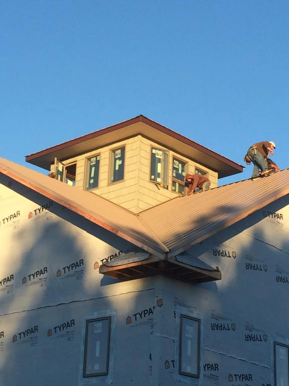 Roofers working around a rooftop cupola on a new metal roof at sunset — Roof Waterproofing in Lumberton by Roofing Brothers